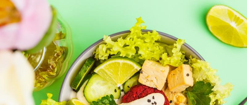 Vegan buddha bowl with beetroot meatballs, vegetables, tahini dressing and baked tofu on green background.